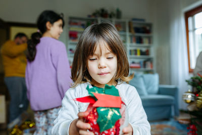 Little child holds christmas decoration in hands with family behind