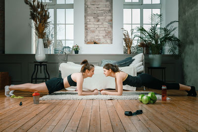 The young women goes in for sports at home. sporty women with black hair makes a plank, watches 