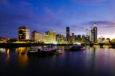 Illuminated buildings by river against sky in city at night