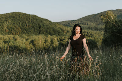 Beautiful woman standing amidst grass against sky