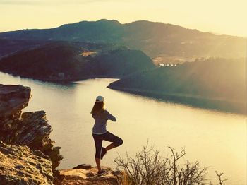 Young woman standing by lake against sky during sunset