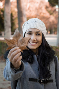 Portrait of a young latin woman smiling. she's holding the typical autumn deciduous leaf.