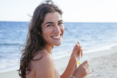 Portrait of smiling woman drinking water from beach