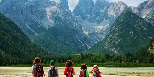 Rear view of children standing against mountains at lakeshore