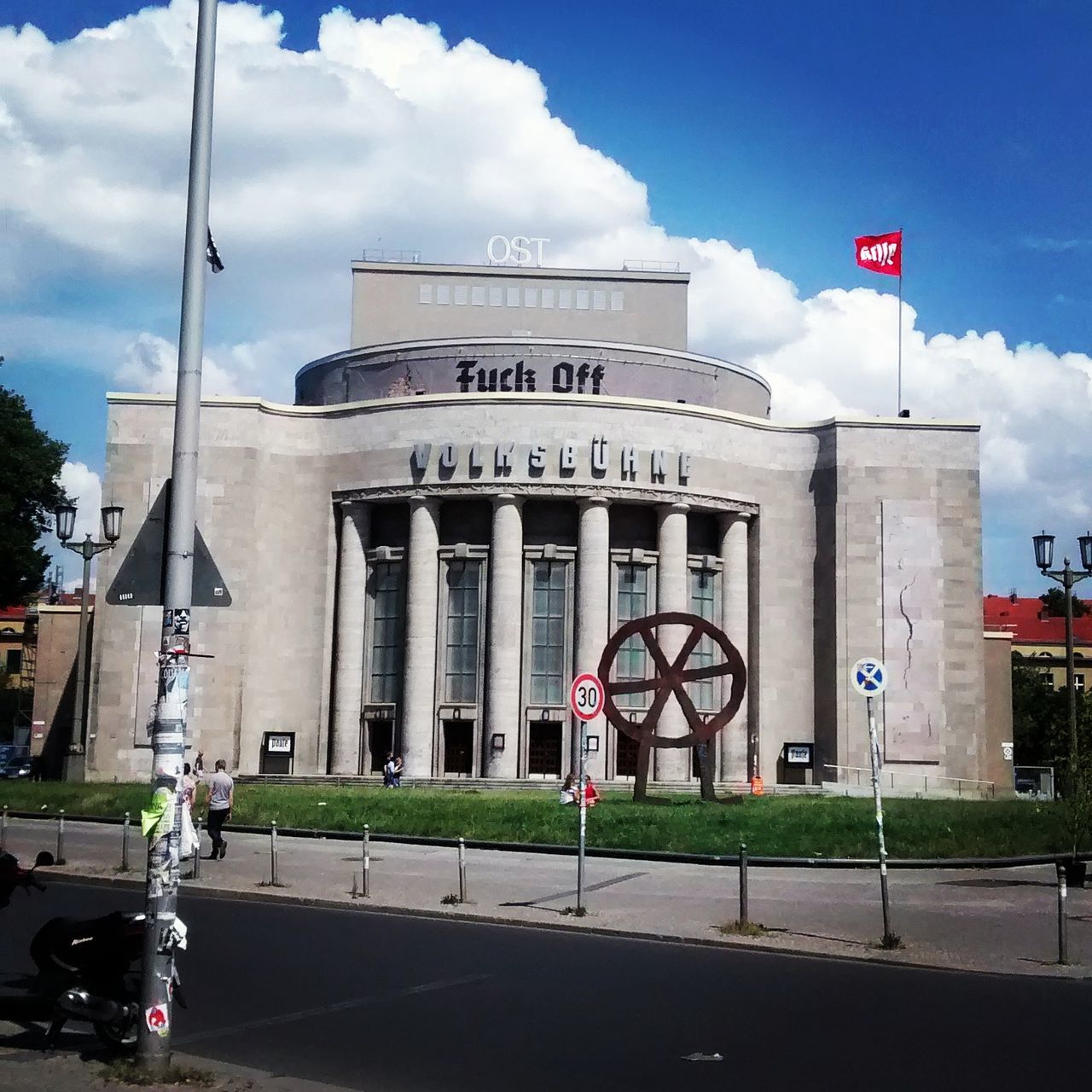 architecture, built structure, text, western script, building exterior, sky, road sign, communication, information sign, cloud - sky, street, road, guidance, sign, transportation, day, flag, cloud, low angle view, city