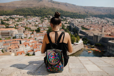 Rear view of woman on retaining wall against cityscape