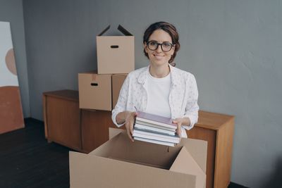 Portrait of young woman holding box while standing against white background