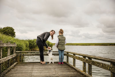 Mother and daughter standing on jetty at a lake with dog