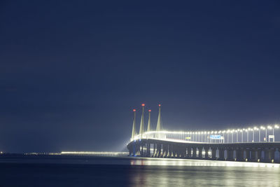 Illuminated bridge over sea against sky at night