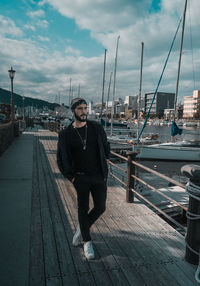 Portrait of young man standing on harbor against sky