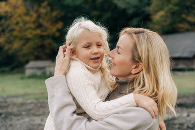 Mom holds in her arms and hugs a little blond cheerful daughter.