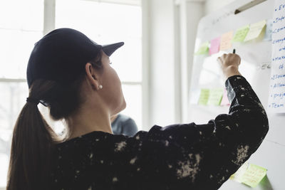 Rear view of woman checking adhesive notes on whiteboard in creative office