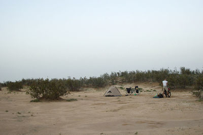 People sitting on sand dune against clear sky