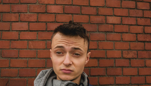 Young man making face against brick wall