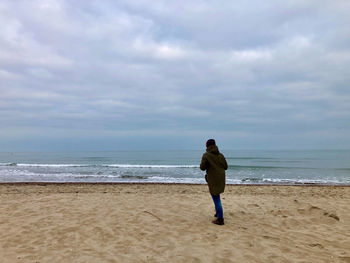 Rear view of woman standing in wind on beach against sky