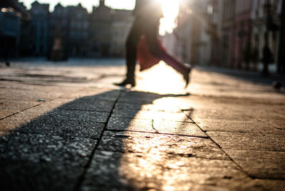 Low section of man walking on cobbled street in city during sunny day