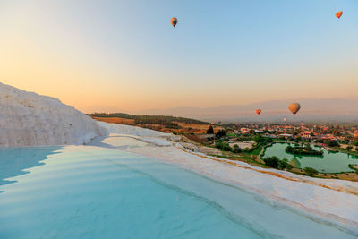 Hot air balloons flying over sea against sky during sunset