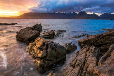 Scenic view of sea and mountains against cloudy sky during sunset