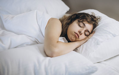 Young girl sleeping in white bed with pillows