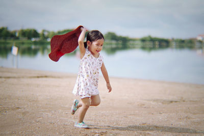 Playful girl holding sun hat while running at beach