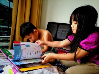 Siblings studying on bed at home