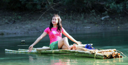 Portrait of smiling young woman sitting on bamboos in lake
