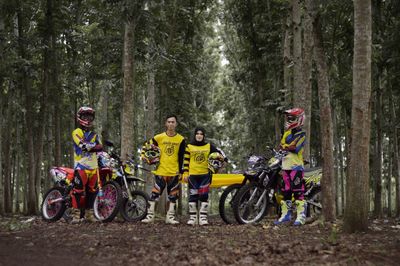 Portrait of friends with motorcycles standing against trees in forest