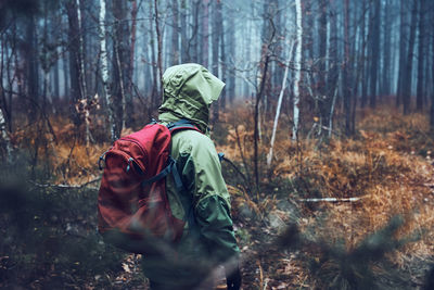 Woman with backpack wandering in a forest on autumn cold day