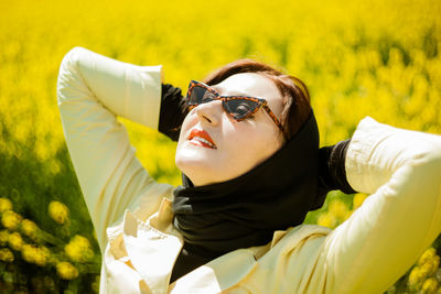 Portrait of stylish woman wearing sunglasses among a blooming yellow field under a bright spring sky