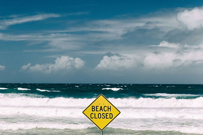 Warning sign on beach against sky