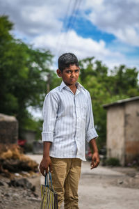 Portrait of young man standing on road against cloudy sky