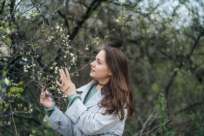 Beautiful girl with long hair in a grey trench coat outdoors in cherry blossoms in spring