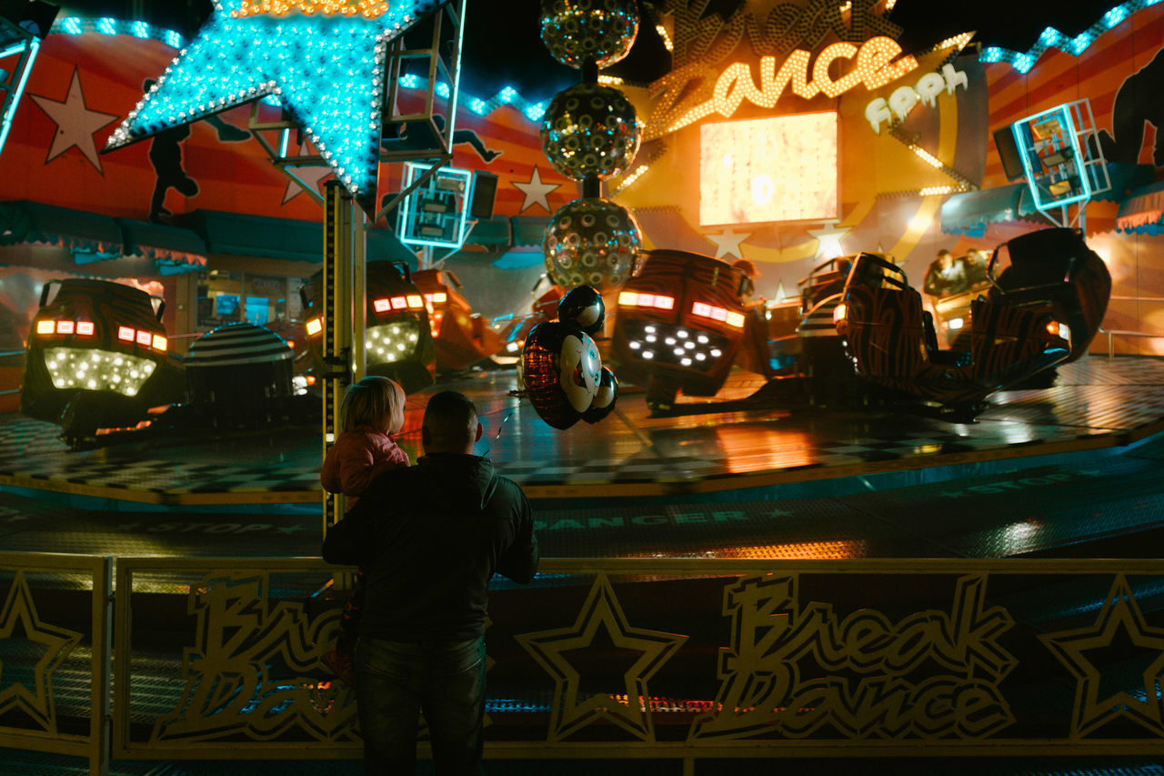 illuminated, night, real people, men, people, city, rear view, lighting equipment, standing, amusement park, leisure activity, adult, architecture, lifestyles, decoration, retail, restaurant, business, outdoors