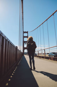 Rear view of woman walking on bridge against blue sky