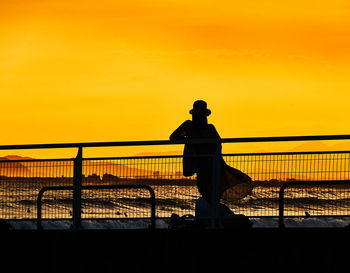 Silhouette women standing on bridge against sky during sunset