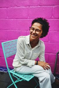 Portrait of smiling young woman sitting on chair against wall