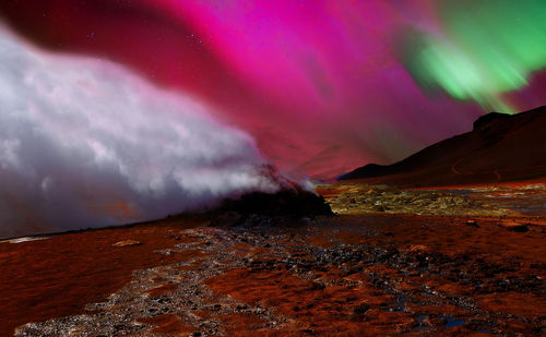 Smoke emitting from volcanic landscape against pink sky