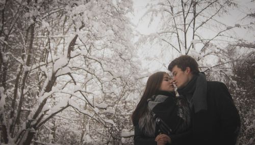 Low angle view of couple face to face standing in forest during winter