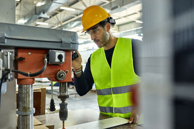 Worker operating drill in factory