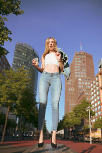 Low angle portrait of woman levitating against buildings