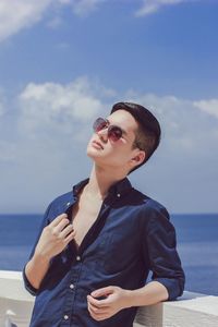 Handsome man standing by retaining wall against sky on sunny day