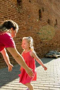 Full length of mother and daughter standing against brick wall