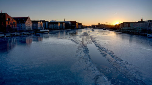 River amidst buildings against sky during sunset