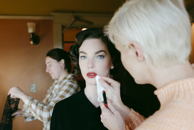 Portrait of young woman with beautician adjusting her lipstick at home
