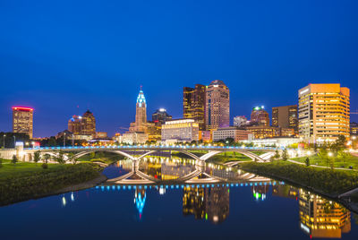 Illuminated buildings by river against clear blue sky at night