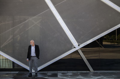 Portrait of adult man in suit against glass wall in business district