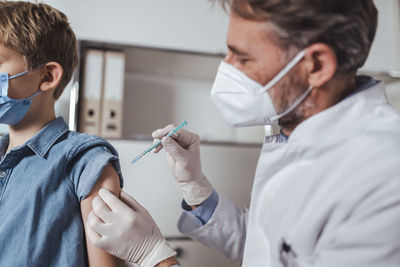 Doctor in face mask administering boy with covid-19 vaccine