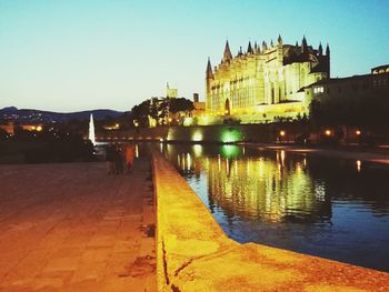 Illuminated buildings by river against sky at dusk