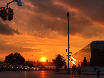 Silhouette city street against orange sky