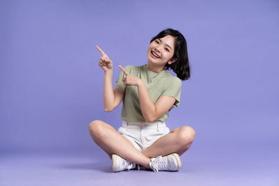 Young woman using mobile phone while sitting against blue background